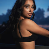 Woman in a black bikini with a tattoo on her back against a dark background