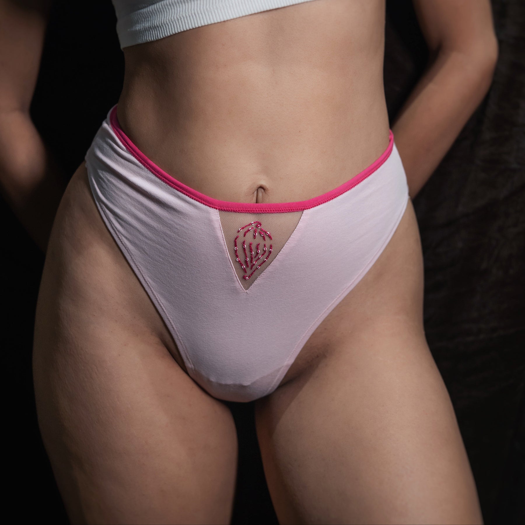 Person wearing a white sports bra and pink underwear with a dark background