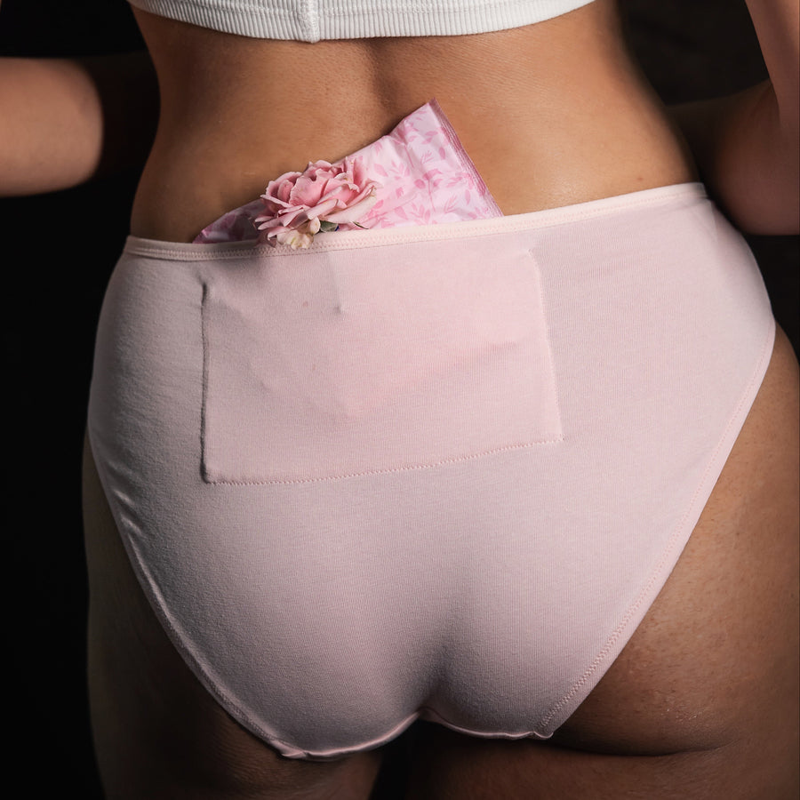 Person wearing light pink high-waisted underwear with a floral pocket on a dark background