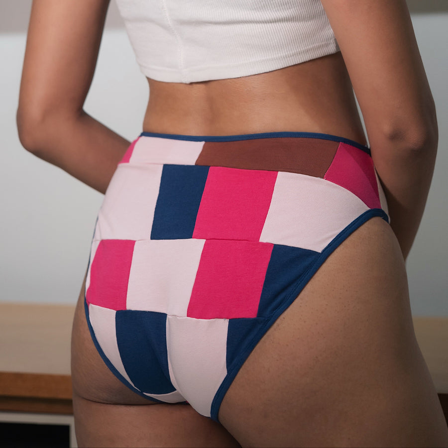 Woman wearing a white top and colorful patterned underwear in a room with a painting on the wall.