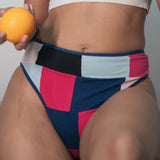 Woman in sports bra and colorful underwear holding an orange in front of a cow painting.