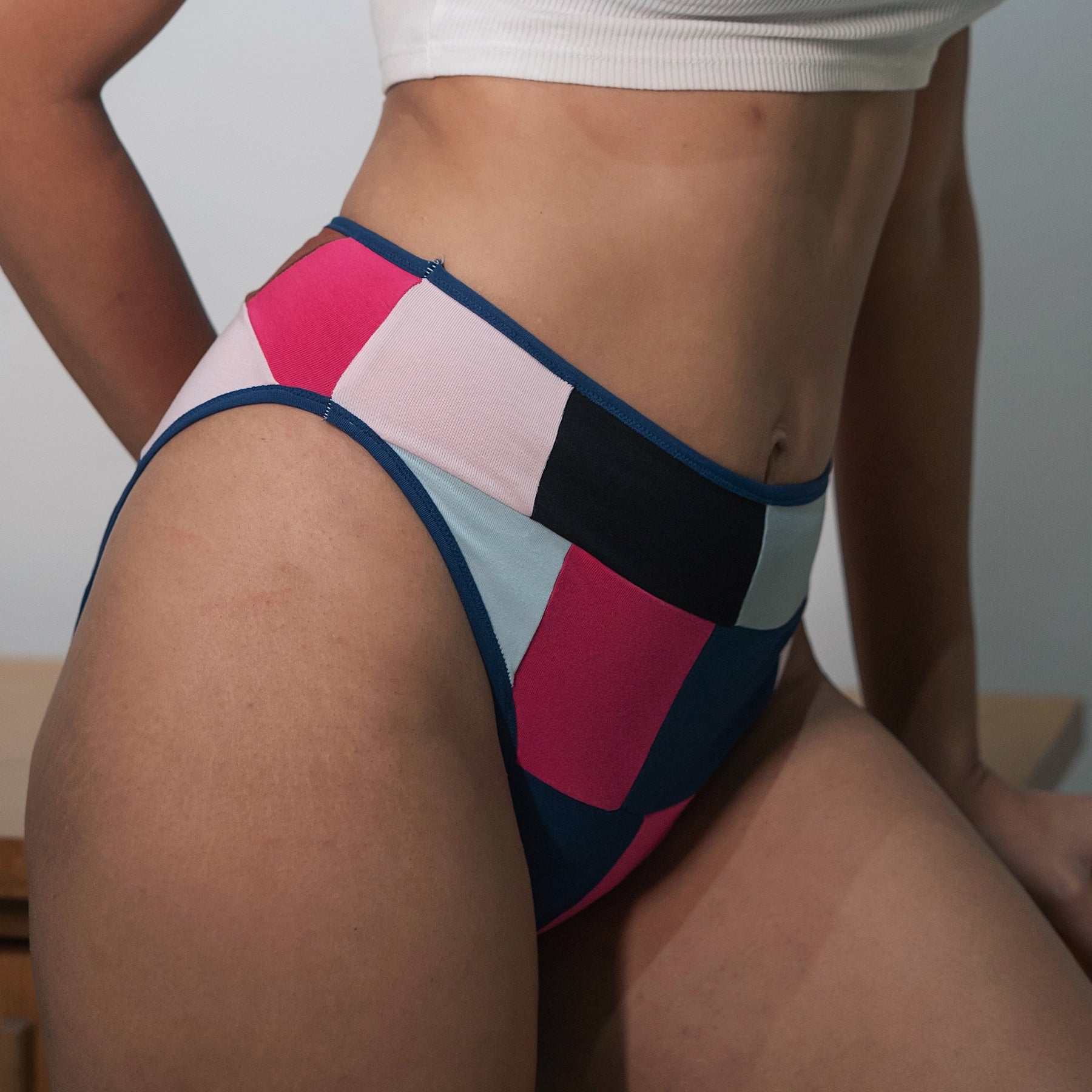 Woman in a white sports bra and colorful patterned underwear standing in front of a painting of cows.