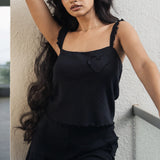 Woman in a black dress standing against a light-colored wall.