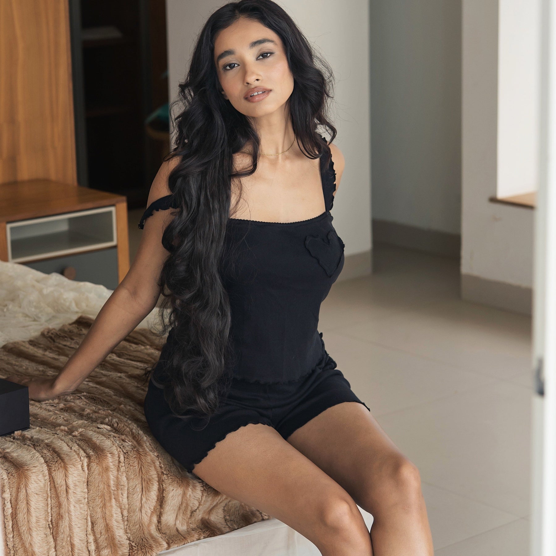 Woman in black lingerie sitting on a bed in a bedroom.